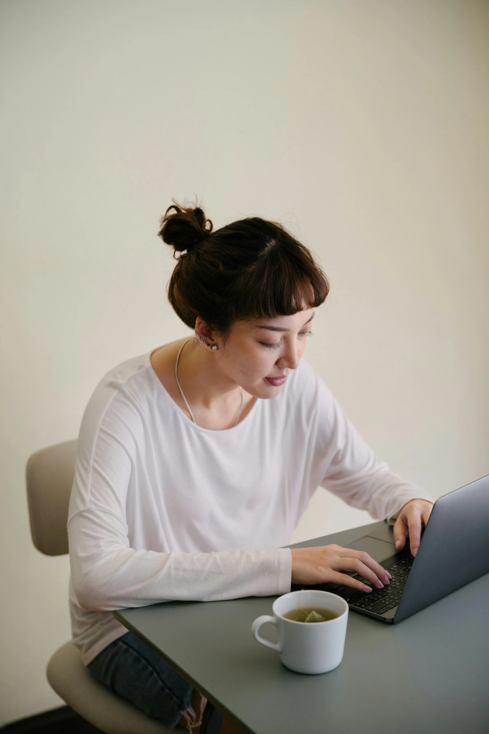 a woman sitting at a table using a laptop computer, a portrait, pexels contest winner, wearing a light shirt, japanese, slightly minimal, androgynous person