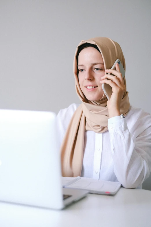 a woman sitting at a table talking on a cell phone, inspired by Maryam Hashemi, pexels, hurufiyya, white helmet, brown and white color scheme, laptop, malaysian