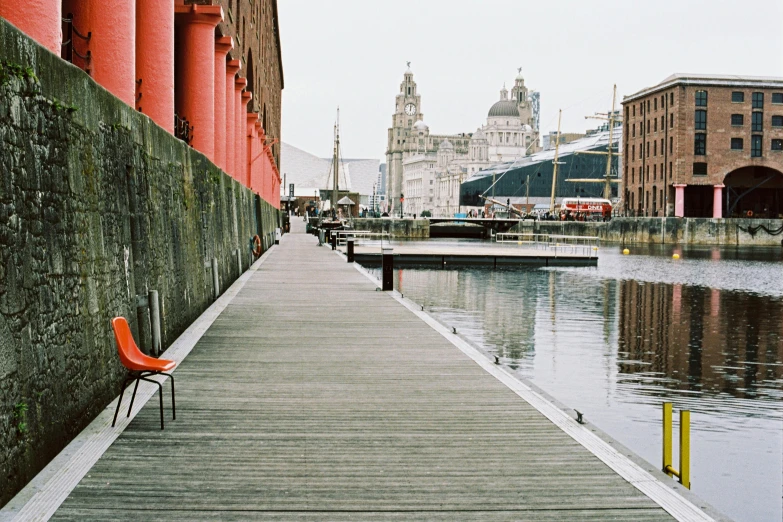 a red chair sitting on a dock next to a body of water, inspired by Thomas Struth, pexels contest winner, hyperrealism, liverpool football club, photograph of the city street, moody : : wes anderson, zeppelin dock