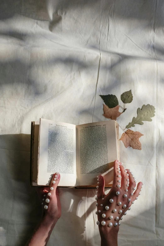 a person laying on a bed reading a book, by Lucia Peka, pexels contest winner, romanticism, dried leaves, hands reaching for her, books covered in jewels, white and pink cloth