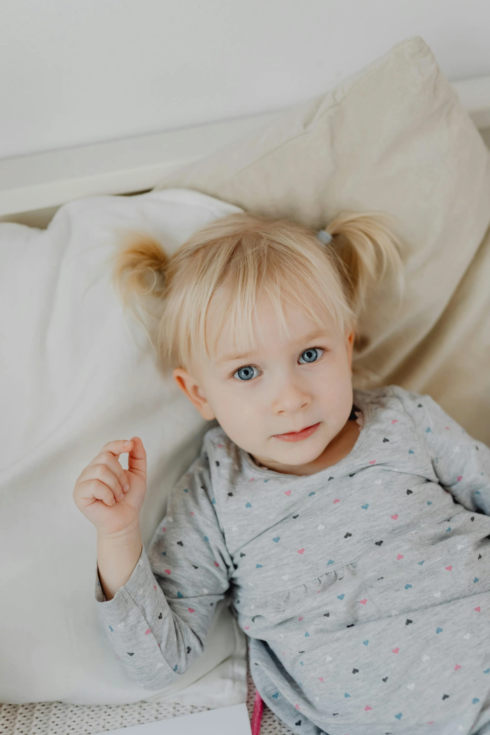 a little girl laying on top of a bed, soft features, holding it out to the camera, ear, a blond