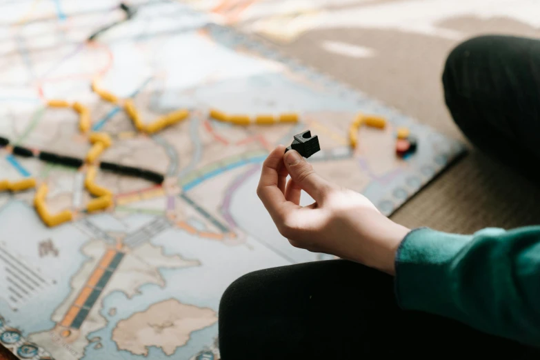 a person sitting on the floor playing a board game, by Kristian Zahrtmann, pexels contest winner, train far, game map, holding it out to the camera, anna nikonova