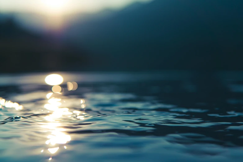 the sun is setting over a body of water, inspired by Elsa Bleda, bokeh photograph, blue water, low-angle shot, dimly - lit