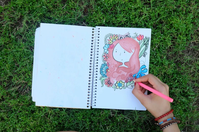a person is drawing a picture on a notebook, by Amelia Peláez, fully colored, in the grass, girl sketch, coloring book style