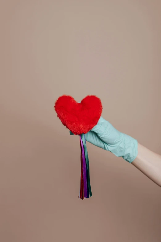 a person in blue gloves holding a red heart, an album cover, inspired by Méret Oppenheim, trending on pexels, stuffed animal, tassels, healthcare worker, colorful aesthetic