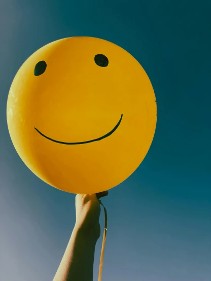 a person holding a yellow smiley face balloon, by Niko Henrichon, trending on pexels, happening, happy tones, paul barson, serene smile, background image