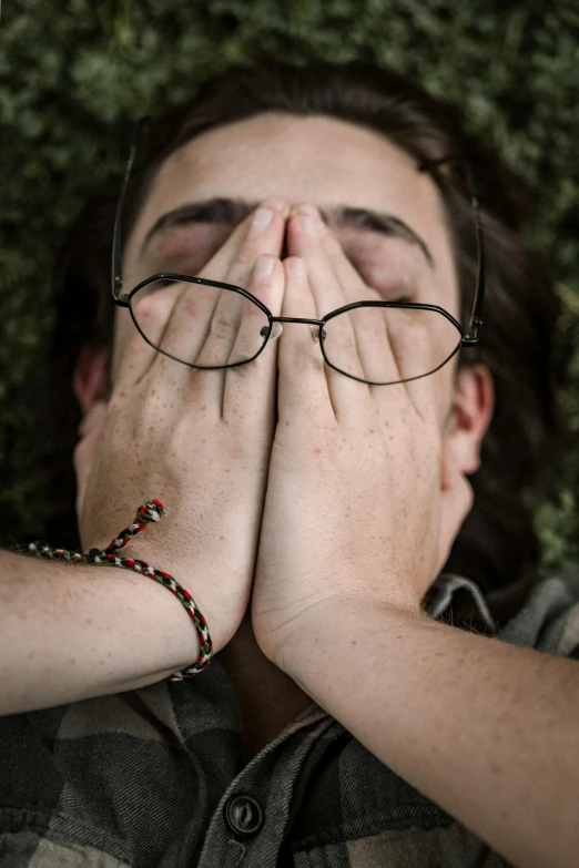 a man laying on the ground covering his face with his hands, trending on pexels, girl with glasses, religious, pleading face, full frame image