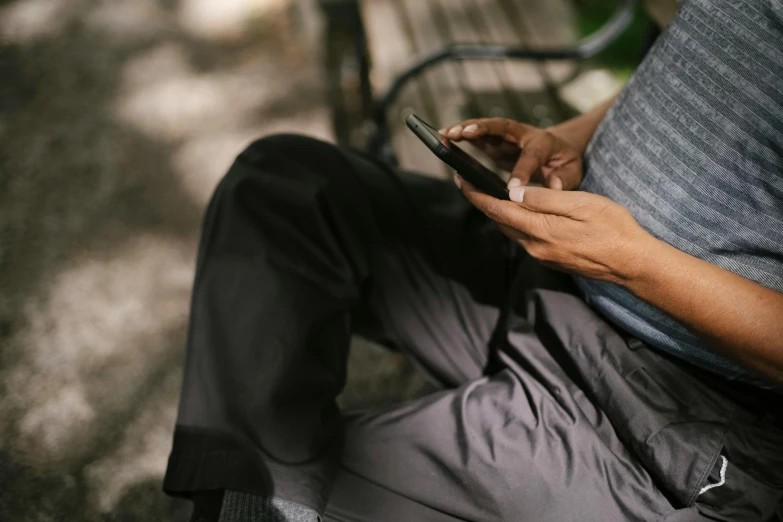 a man sitting on a bench using a cell phone, trending on pexels, connection rituals, sitting in the garden, unreadable text, rounded corners