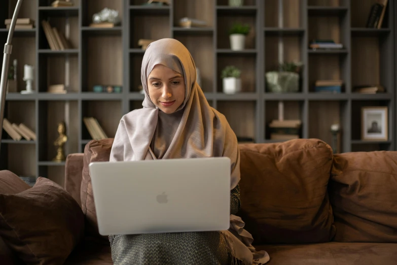 a woman sitting on a couch using a laptop, inspired by Maryam Hashemi, trending on pexels, hurufiyya, islamic, medium shot portrait, beige, malaysian