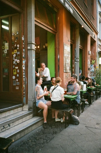 a group of people sitting outside of a restaurant, kreuzberg, green alleys, ignant, metropolitan