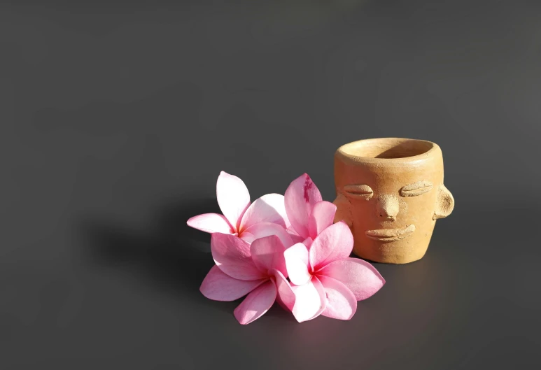 a vase sitting on top of a table next to a flower, a surrealist sculpture, inspired by Robert Mapplethorpe, unsplash, asian face, wood cups, pink zen style, background image