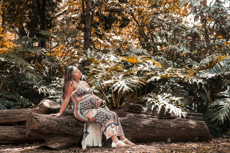 a woman sitting on a log in the woods, a portrait, unsplash, elegant tropical prints, pregnant, avatar image, são paulo