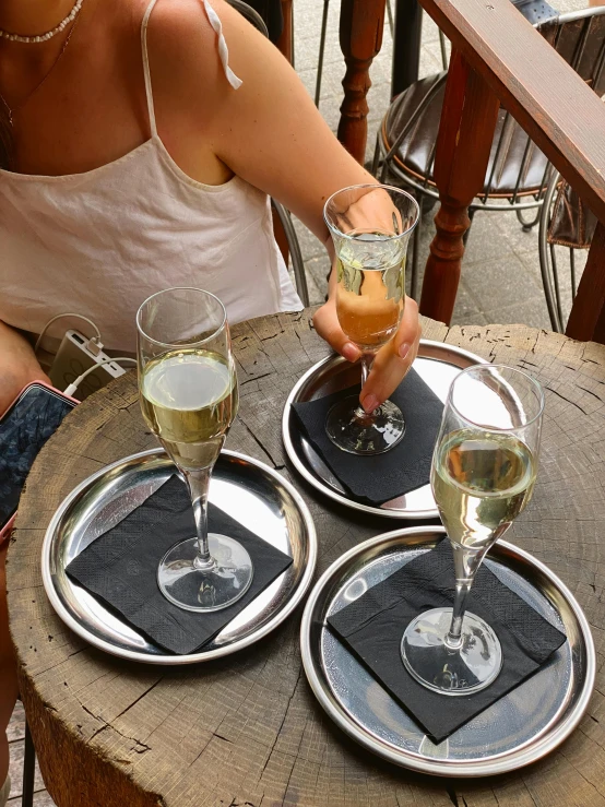 a woman sitting at a table with two glasses of wine, charcoal and champagne, silver platter, in chippendale sydney, silver small glasses