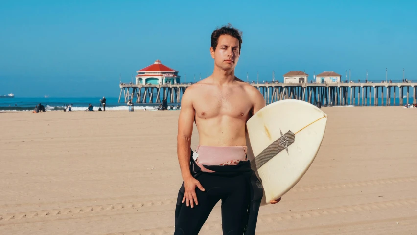 a man standing on a beach holding a surfboard, physical : tinyest midriff ever, nonbinary model, white cummerbund, flume