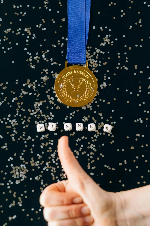 a person giving a thumbs up in front of a medal, an album cover, by Julia Pishtar, pexels contest winner, renaissance, glittering stars scattered about, award winning dish, navy, close-up from above