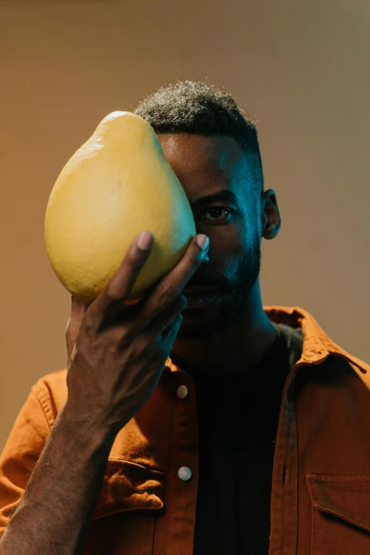 a man holding a pear in front of his face, an album cover, inspired by Paul Georges, trending on unsplash, african man, clear julian lage face, yellow helmet, movie still