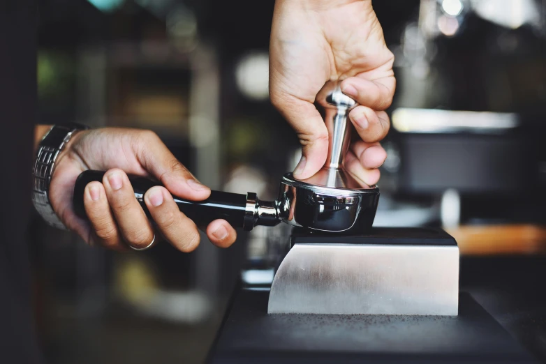 a close up of a person using a coffee grinder, an engraving, trending on unsplash, aussie baristas, thumbnail, stainless steal, stitching