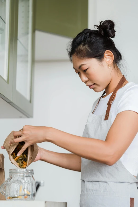 a woman standing in a kitchen preparing food, inspired by Ruth Jên, holding a gold bag, dried herbs, darren quach, carefully designed