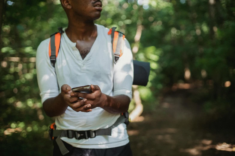 a man standing in the woods holding a cell phone, trending on unsplash, man is with black skin, hiking clothes, avatar image, teaching