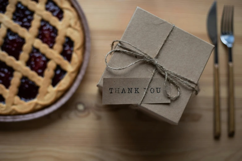 a box sitting on top of a table next to a pie, pexels contest winner, private press, thank you, detailed string text, label, mini