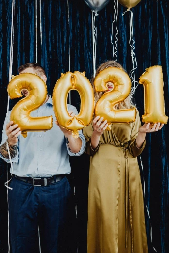 a man and a woman holding balloons in the shape of the numbers 2012, trending on pexels, happening, gold, college, 2021, 🚿🗝📝