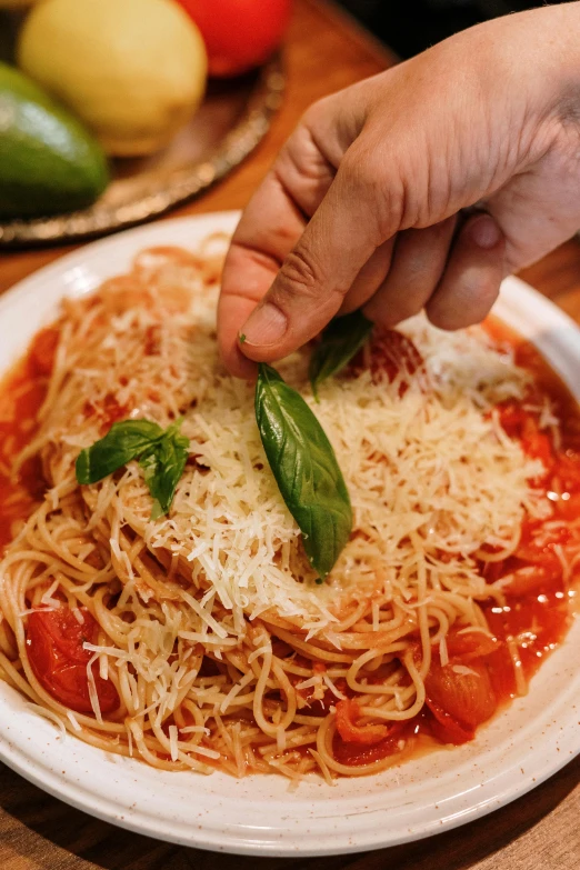 a person putting a piece of parmesan cheese on top of a plate of spaghetti, basil gogos, authentic, tomato sauce, very detailed »