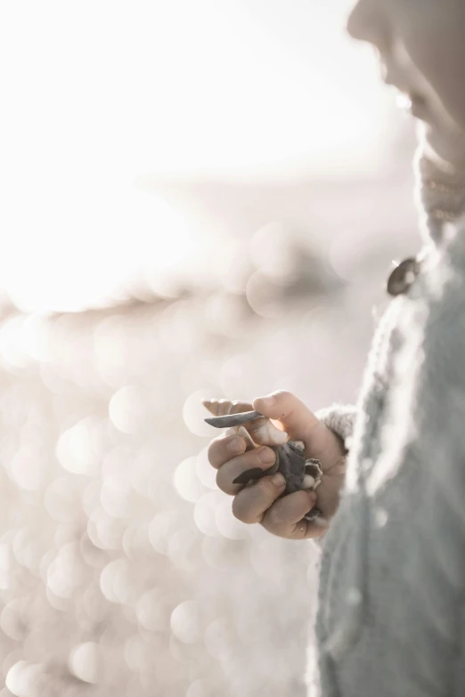 a close up of a person holding a cell phone, by Adam Marczyński, trending on unsplash, minimalism, seaglass, soft light of winter, seeds, silver light