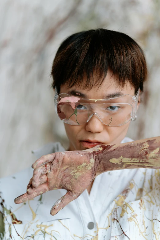 a close up of a person with dirt on their hands, an album cover, inspired by Fei Danxu, gutai group, wearing gold glasses, androgynous person, marbling, in an action pose