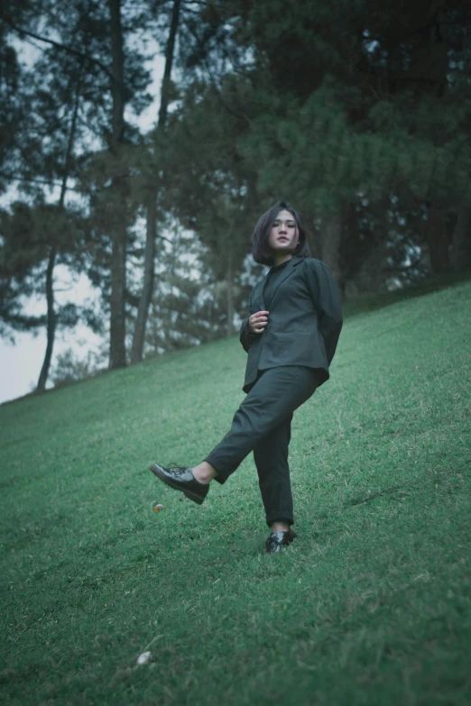 a woman standing on top of a lush green field, an album cover, by Basuki Abdullah, unsplash, grey pants and black dress shoes, wearing a worn out suit, ((portrait)), androgynous person