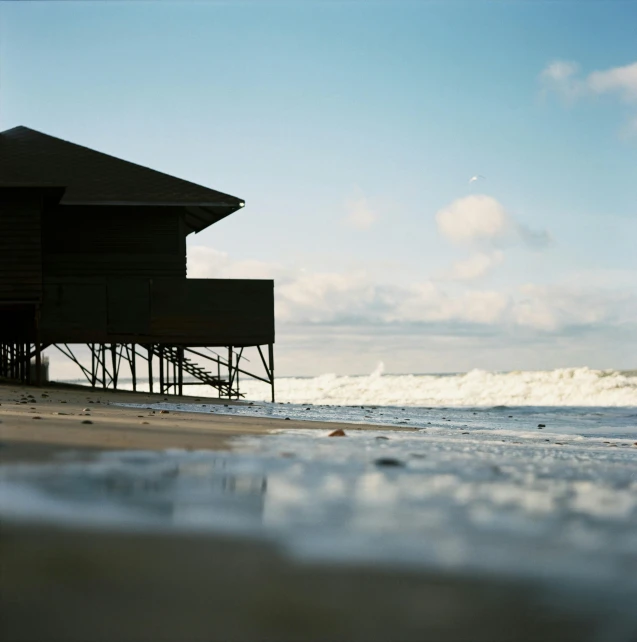 a man riding a surfboard on top of a sandy beach, an album cover, unsplash, photorealism, wooden house, nadav kander, view of sea, pavilion