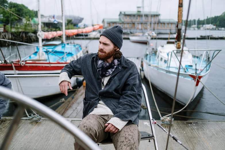 a man that is sitting on a boat, a portrait, unsplash, baggy clothing and hat, harbour, wearing jacket, pendleton ward