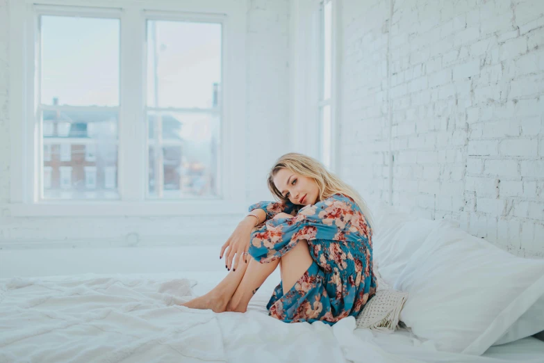 a woman sitting on top of a bed next to a window, a portrait, inspired by Elsa Bleda, trending on pexels, floral clothes, young blonde woman, fullbody photo, photoshoot for skincare brand