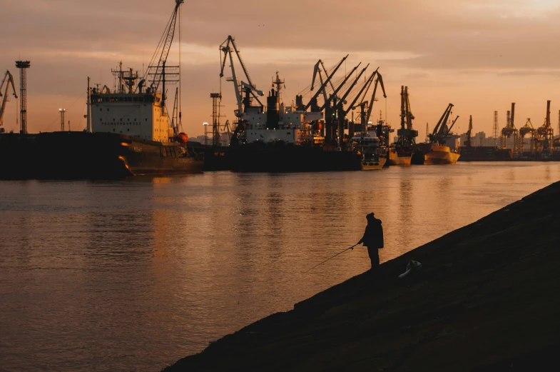 a person standing on a beach next to a body of water, by Matija Jama, pexels contest winner, shipping docks, peter the great, fishing, thumbnail