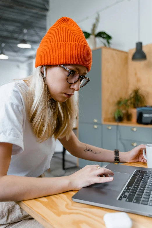 a woman sitting at a table using a laptop computer, trending on pexels, arbeitsrat für kunst, she is wearing a hat, nerdy appearance, thumbnail, 9 9 designs