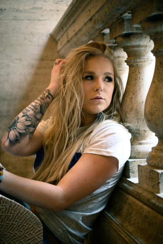 a woman sitting on the steps of a building, a tattoo, kristen bell, on a large marble wall, shot with sony alpha, music