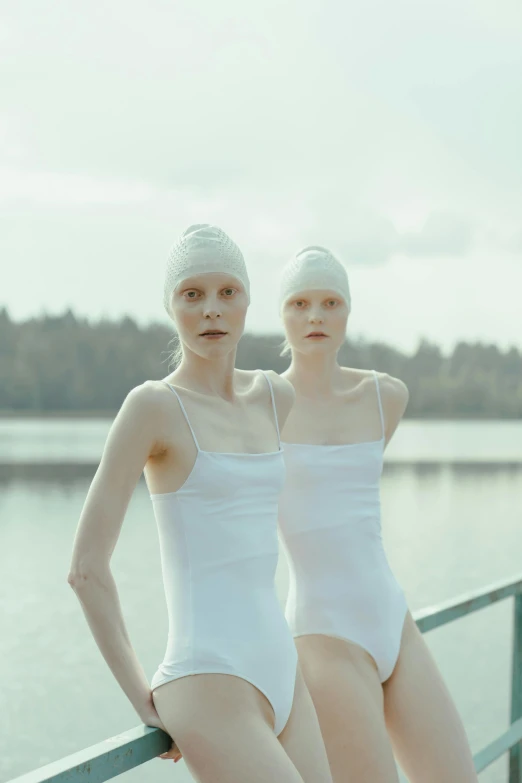 two women standing next to each other near a body of water, inspired by Vanessa Beecroft, unsplash, renaissance, wearing a white bathing cap, intense albino, elle fanning as an android, finland