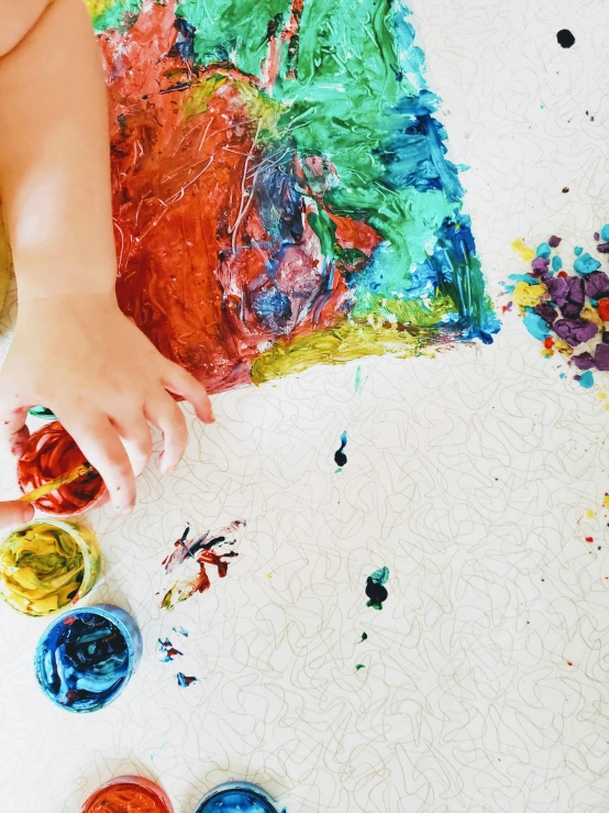 a baby is playing with paints on the floor, a child's drawing, inspired by Sam Francis, trending on unsplash, process art, promo image, hand on table, colorful torn fabric, embossed paint