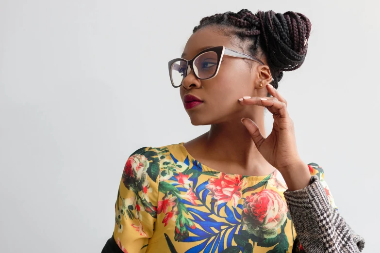 a woman with glasses posing for a picture, by Chinwe Chukwuogo-Roy, trending on pexels, afrofuturism, floral clothes, girl with messy bun hairstyle, square rimmed glasses, thinking pose