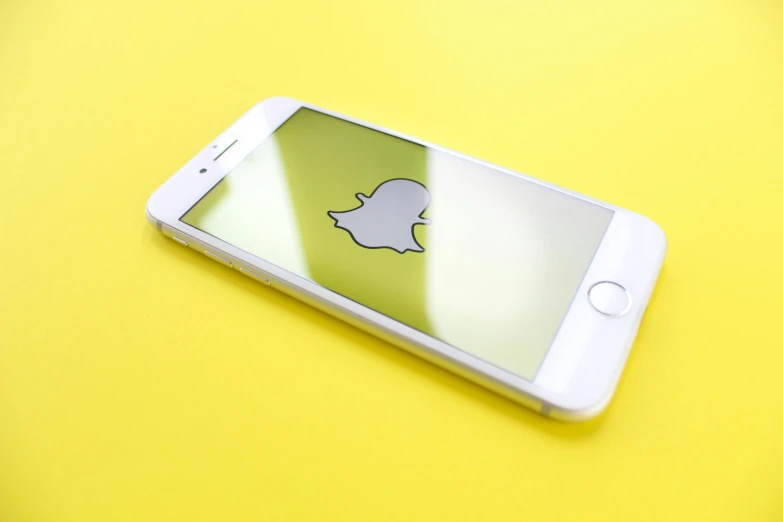 a close up of a cell phone on a yellow surface, a cartoon, trending on unsplash, snapchat, silver and yellow color scheme, square, a wooden