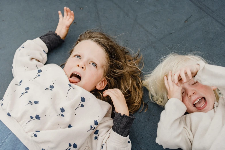 a couple of kids laying on top of a floor, by Will Ellis, pexels contest winner, hair fluttering in the wind, funny faces, sisters, thumbnail