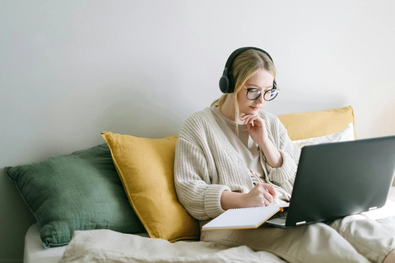 a woman sitting on a bed using a laptop computer, trending on pexels, analytical art, wearing black headphones, avatar image, studious, wearing black rimmed glasses