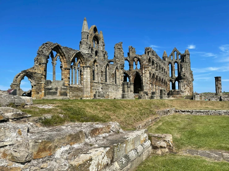 a large stone building sitting on top of a lush green field, pexels contest winner, romanesque, huge support buttresses, coastal, yorkshire, rusty