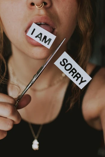 a woman holding a pair of scissors in front of her face, trending on pexels, antipodeans, woman holding sign, forgiveness, stickers, there for i am