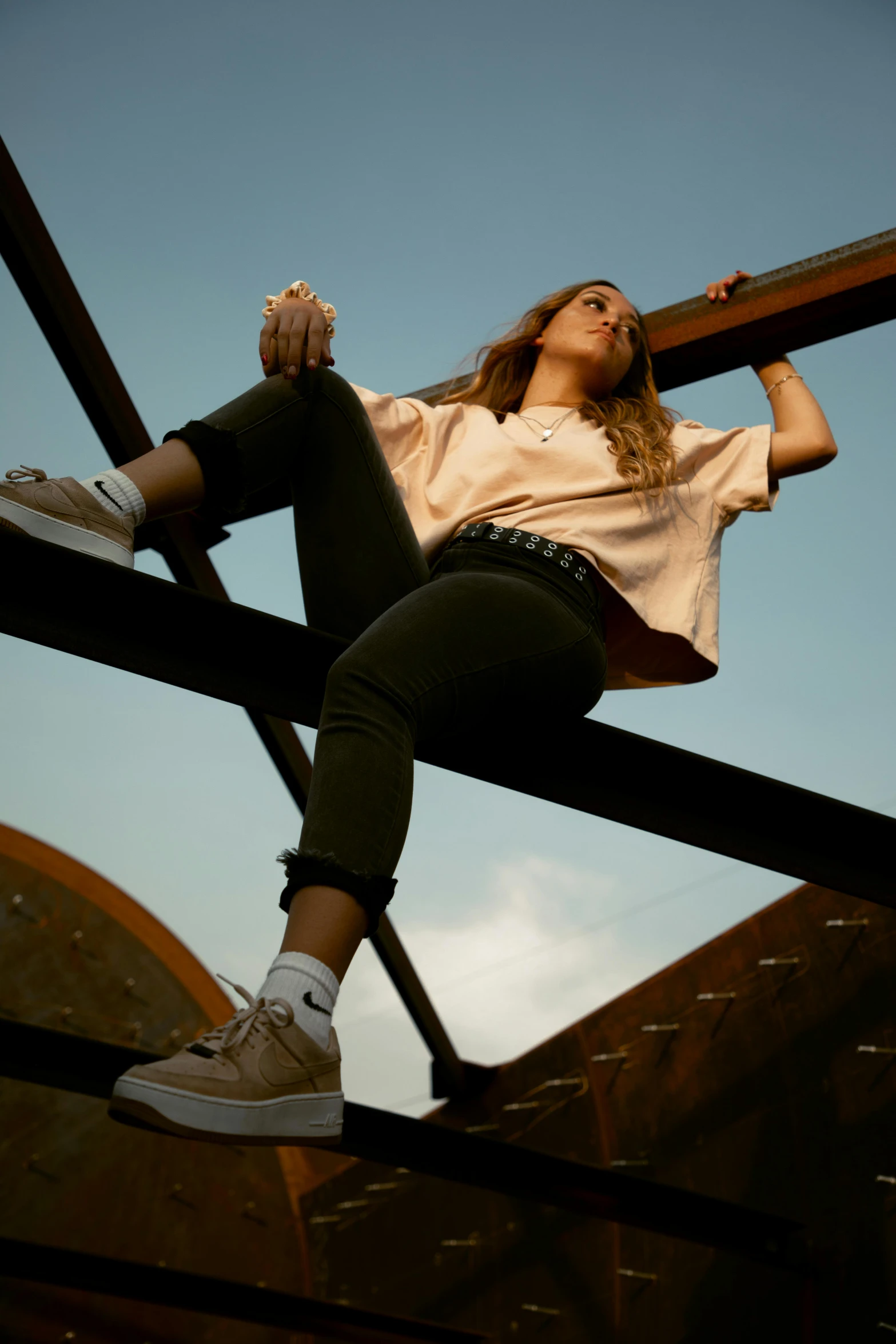 a woman sitting on top of a metal structure, trending on pexels, wearing pants and a t-shirt, caramel. rugged, looking up, teenage