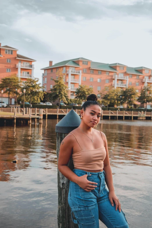 a woman standing on a dock next to a body of water, by Robbie Trevino, mixed race woman, waterfront houses, standing in a city center, tanned