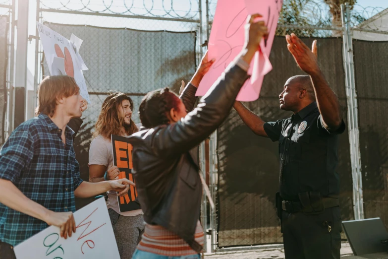 a group of people holding signs in front of a fence, by Carey Morris, pexels contest winner, black arts movement, saluting, arrested, california;, holding a tower shield