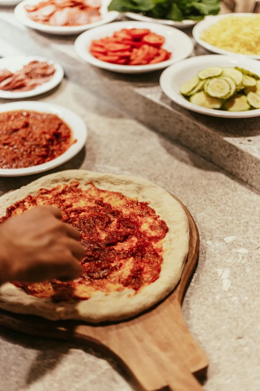 a person is putting toppings on a pizza, by Julia Pishtar, hands on counter, family dinner, mid shot, reds