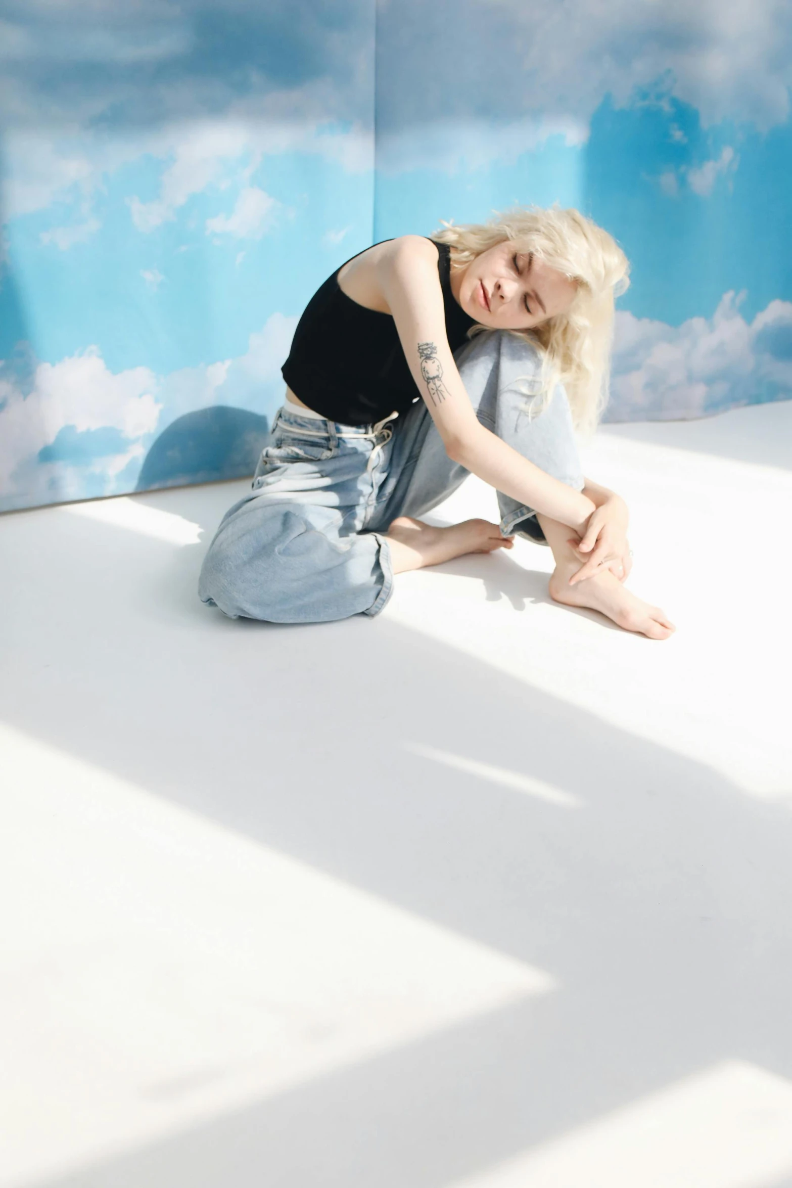 a woman sitting on top of a white floor, an album cover, inspired by Elsa Bleda, photorealism, pale hair, with clouds in the sky, blue jeans, pale fair skin!!