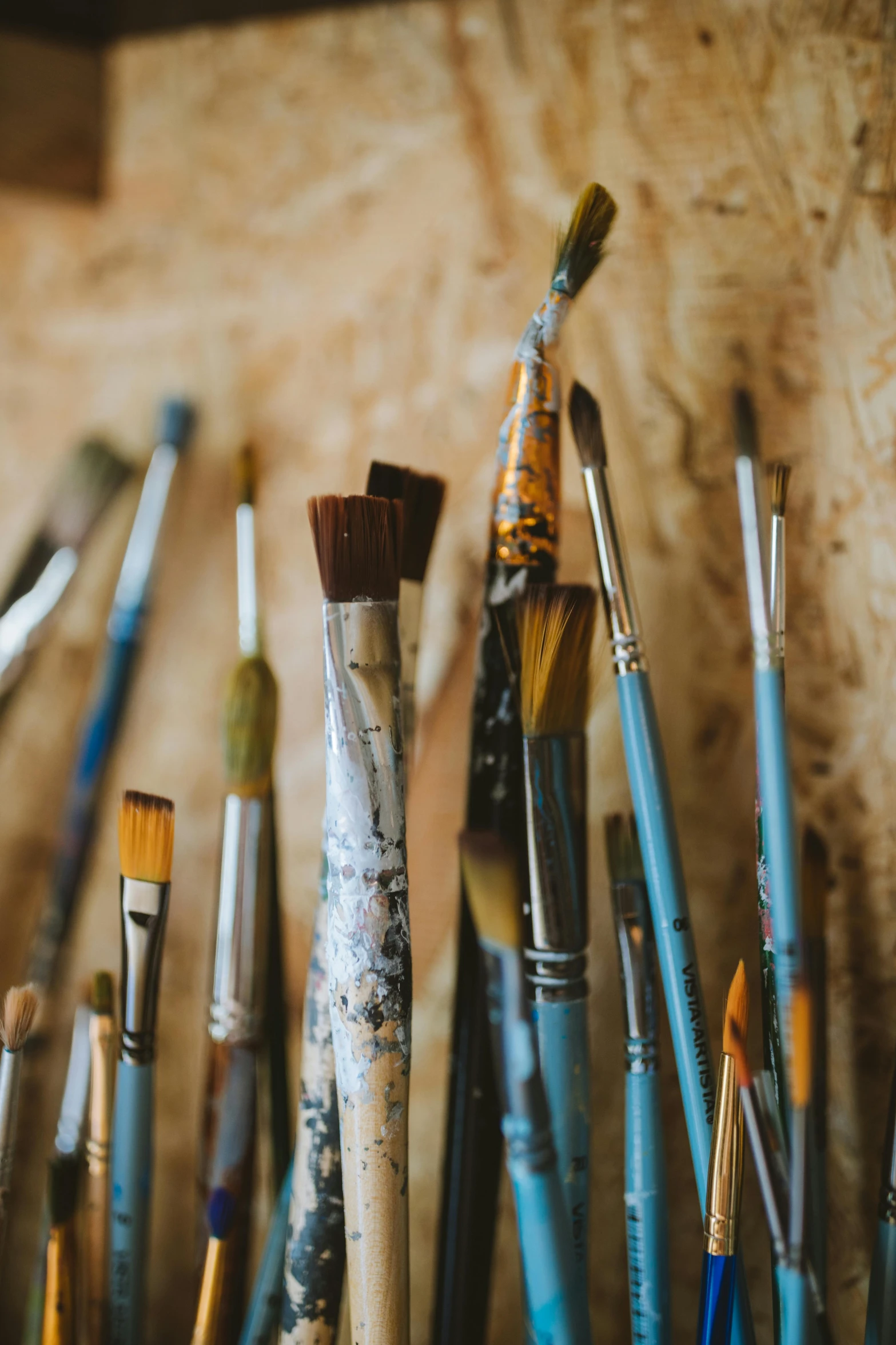 a bunch of paint brushes sitting on top of a table, an oil painting, trending on unsplash, process art, brown, burnt umber and blue, in a workshop, an artistic pose