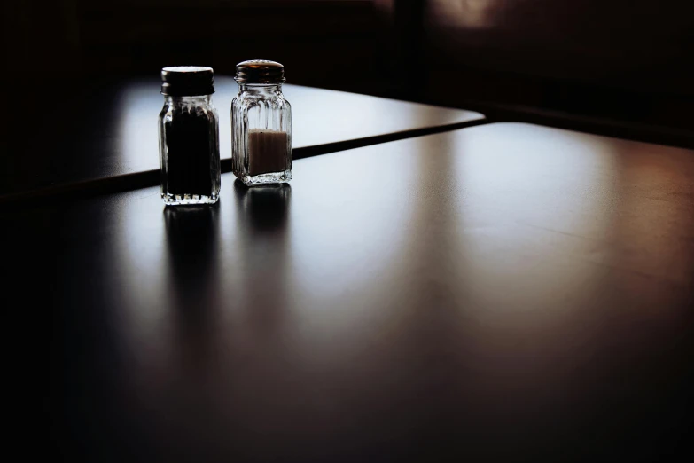 two salt and pepper shakers sitting on a table, unsplash, square, black floor, sitting on a mocha-colored table, lonely